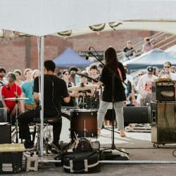 Live outdoor concert performance at a music festival with band playing under a tent, audience enjoying the music, vibrant atmosphere, and sound equipment setup.