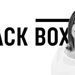 Empowered woman standing in front of Black Box music industry logo, symbolizing innovation and leadership in the music and entertainment technology sector.