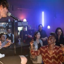 Live music performance at a vibrant nightclub with an enthusiastic audience enjoying the artist's guitar and singing, creating a lively and energetic atmosphere.