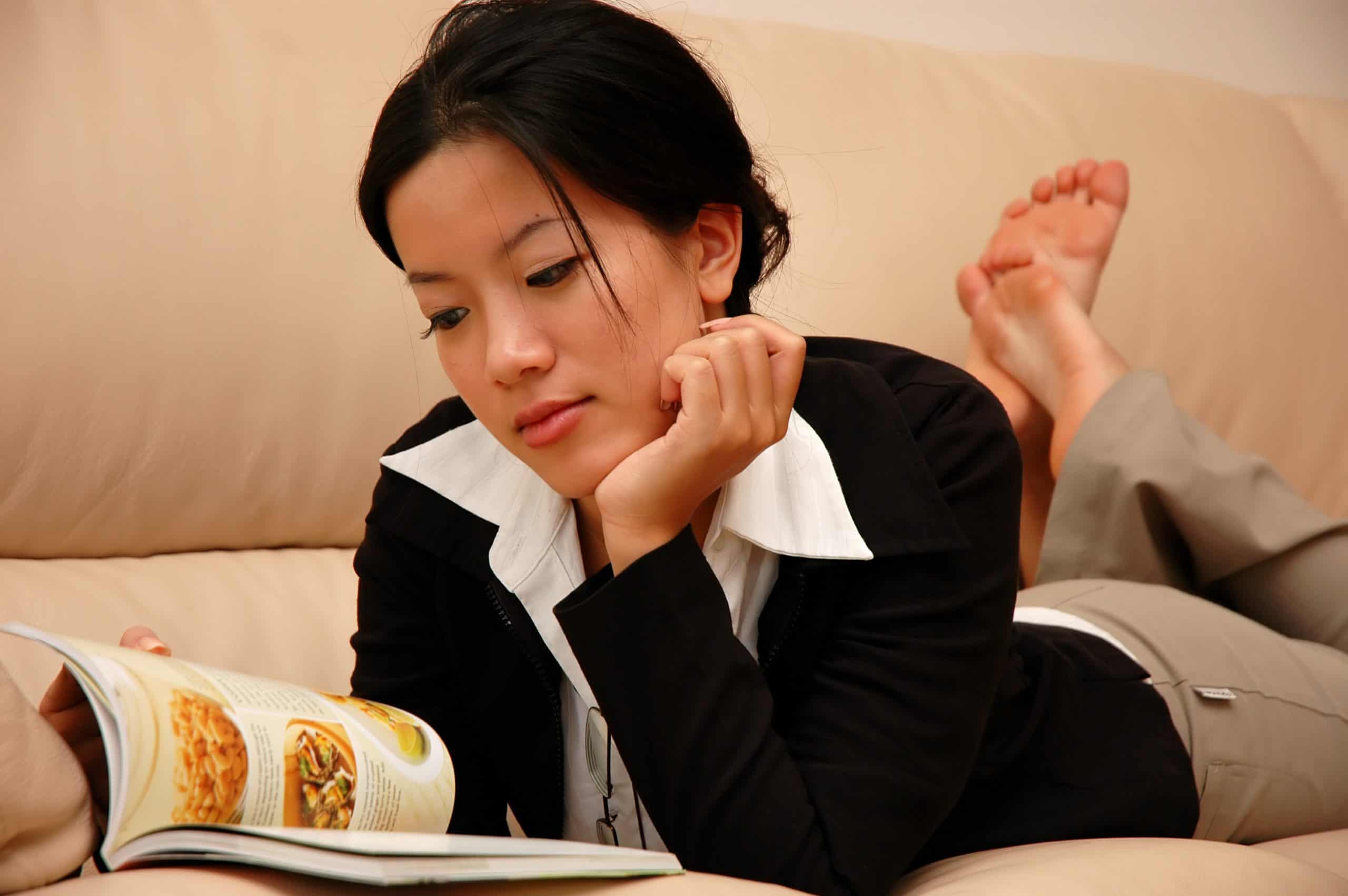 A woman lying on her couch at home, reading about how to date as an introvert.