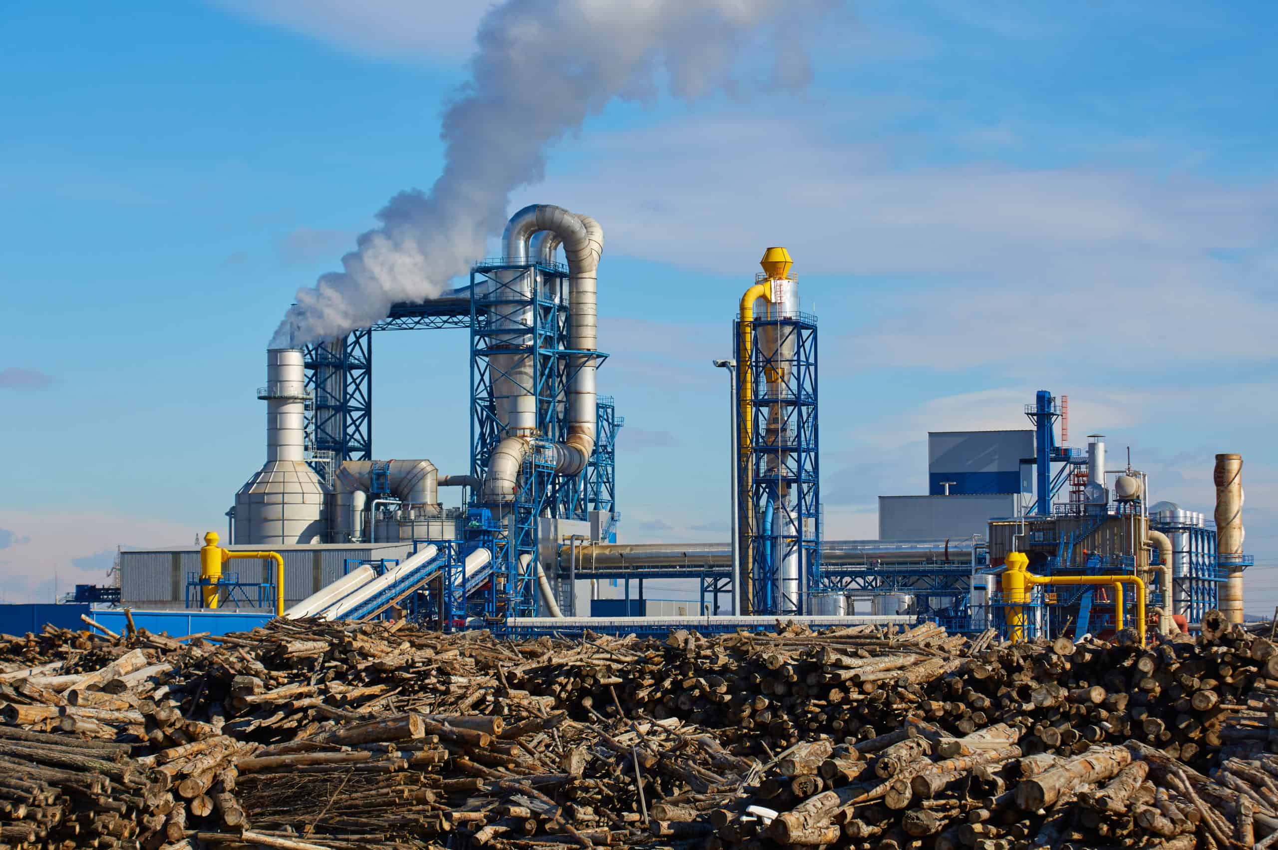 Heavy industrial manufacturing facility with active smokestacks emitting visible emissions surrounded by industrial debris and equipment — major stationary sou…Heavy industrial manufacturing facility with active smokestacks emitting visible emissions surrounded by industrial debris and equipment — major stationary source subject to EPA New Source Review, Title V air permitting, and emissions reduction compliance consulting by EDGE Engineering.
