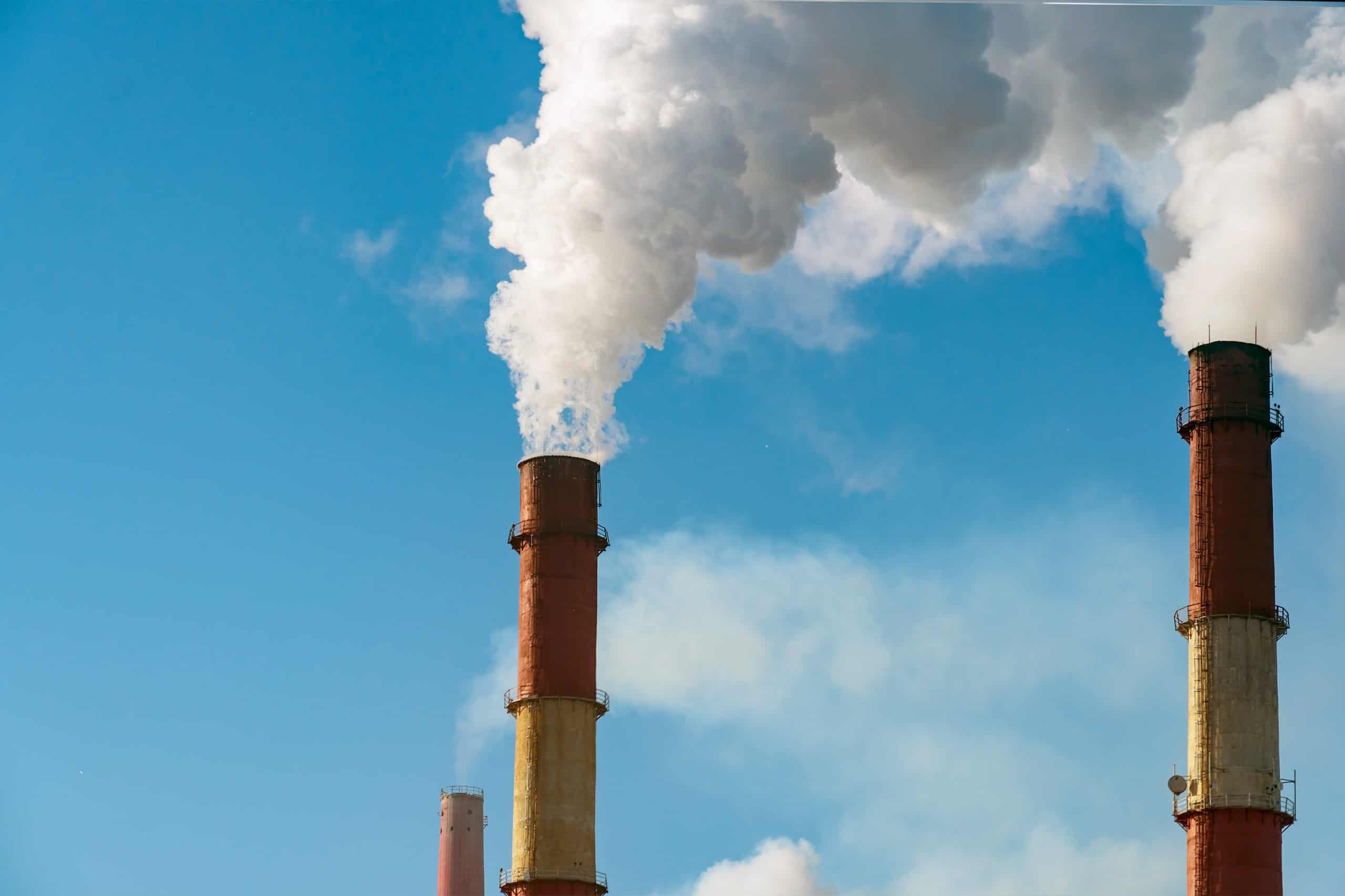 Red and white striped industrial smokestacks releasing steam and emissions against a bright blue sky — coal or natural gas power plant emission sources subject…Red and white striped industrial smokestacks releasing steam and emissions against a bright blue sky — coal or natural gas power plant emission sources subject to EPA Clean Air Act regulations, Title V operating permits, and air quality compliance monitoring by EDGE Engineering.