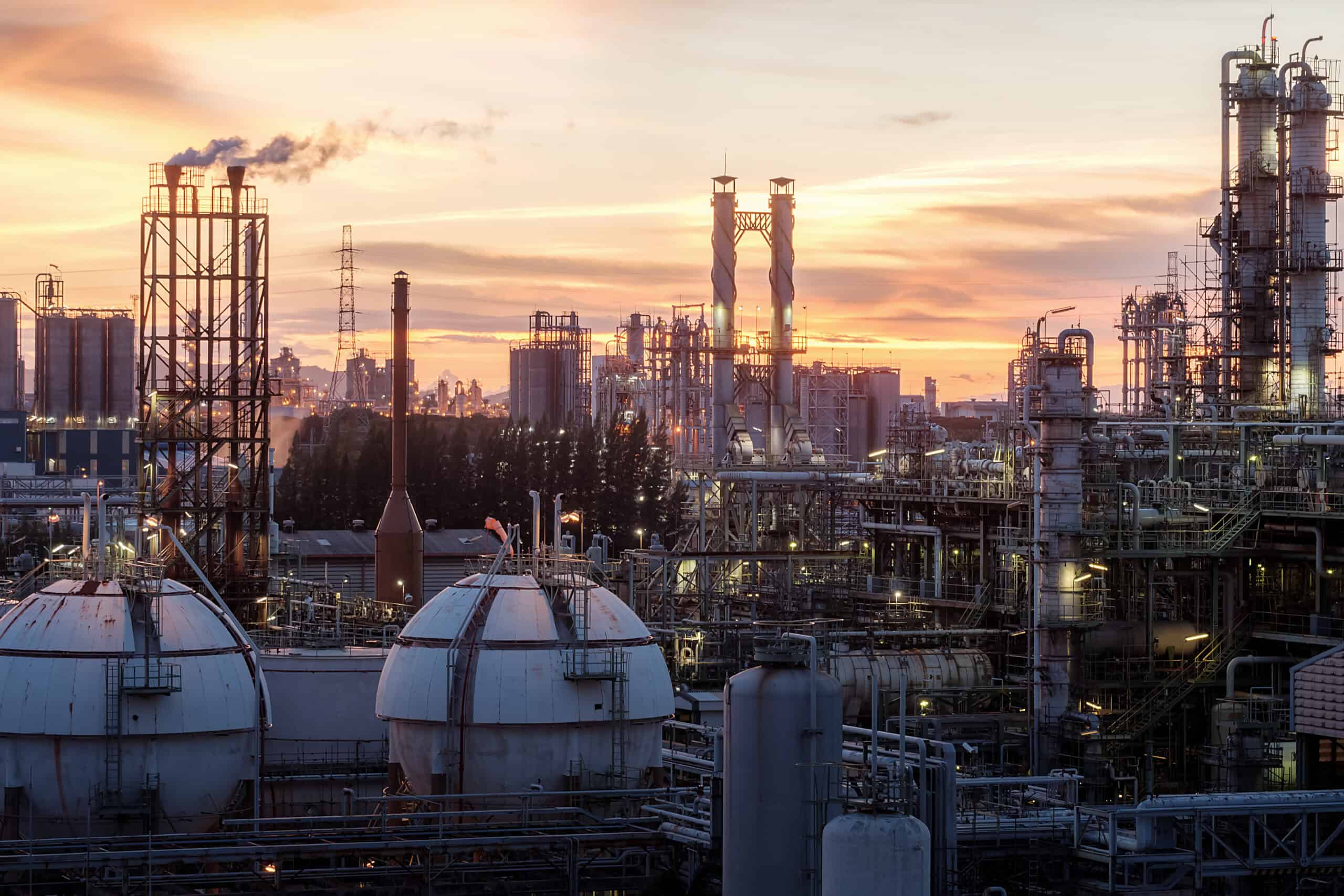 Large petrochemical complex with spherical storage tanks and refinery towers illuminated against a dramatic dusk sky — major stationary emission source requiri…Large petrochemical complex with spherical storage tanks and refinery towers illuminated against a dramatic dusk sky — major stationary emission source requiring Title V air permitting, NSR preconstruction review, and Clean Air Act compliance consulting by EDGE Engineering.