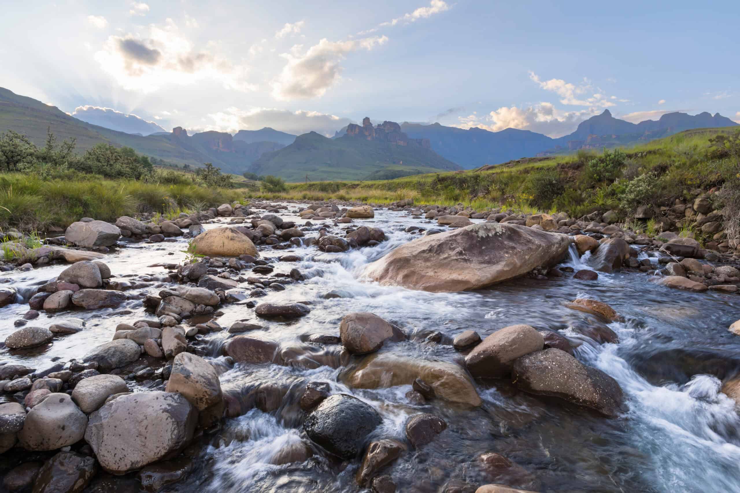 Clear mountain stream flowing over boulders and rocky substrate with peaks and dramatic cloudscape in the background — pristine aquatic habitat requiring Section 404 wetland permitting, water quality assessment, and environmental impact consulting by EDGE Engineering for nearby construction and development projects.