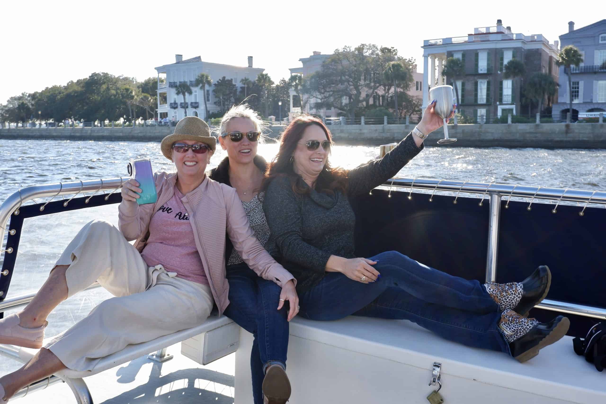 Women raising their glasses on the boat with sun shining down on The Battery. Private charter Charleston, SC