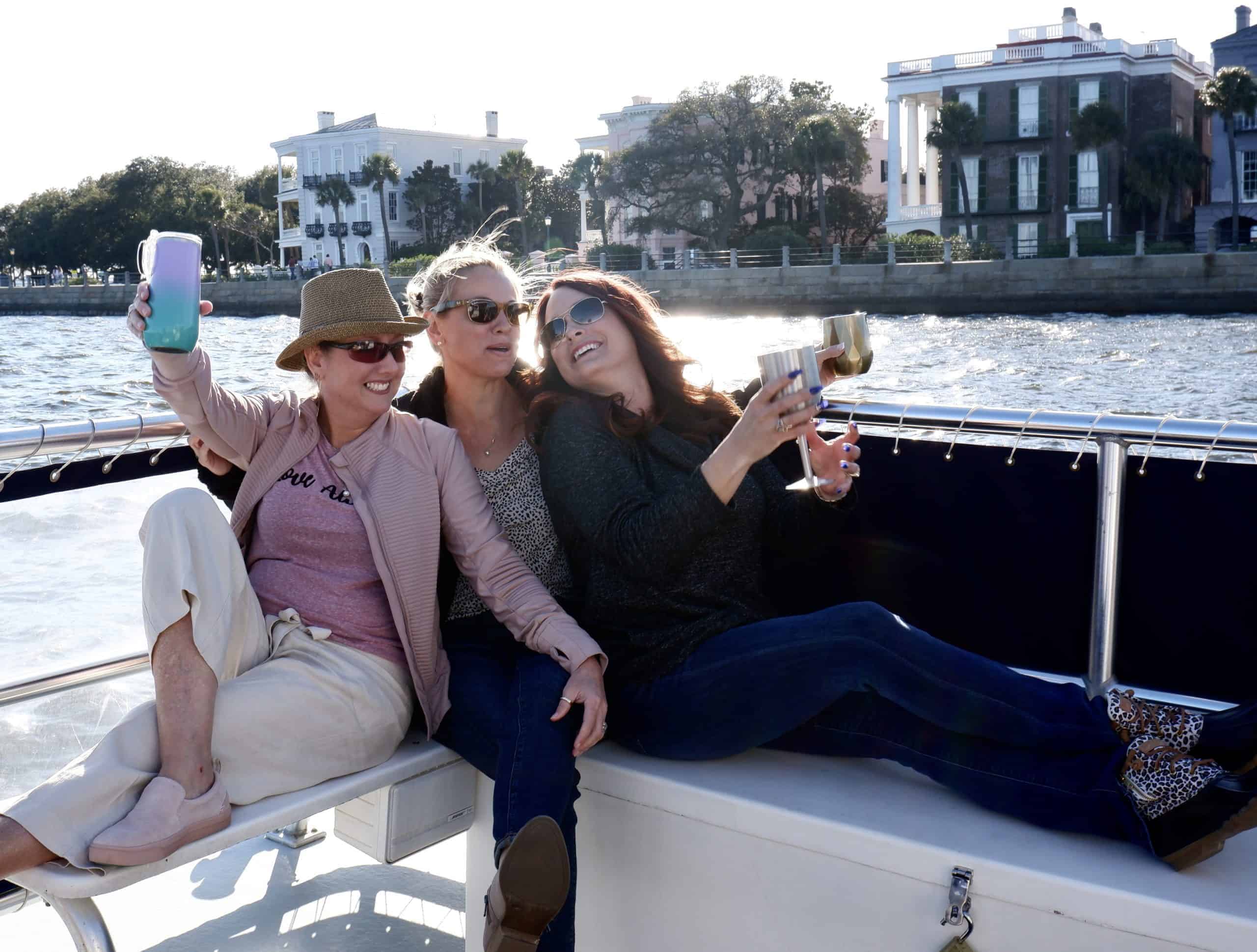 Women raising their glasses together on the boat with sun shining down on The Battery. Private charter Charleston, SC