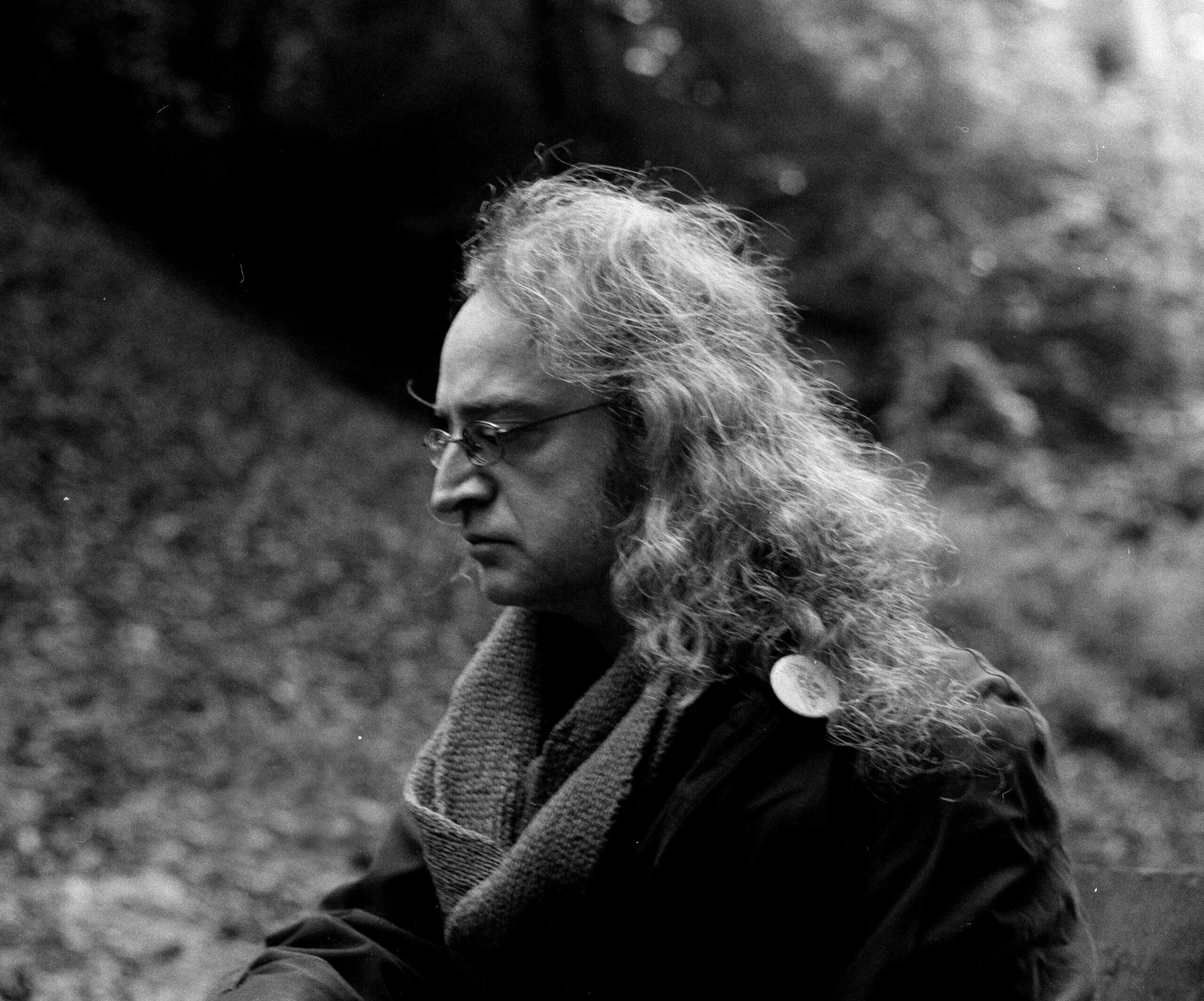 Man outdoors in profile black and white photo, wearing glasses and scarf, contemplative expression, natural background; artistic portrait capturing serenity and introspection for nature and mindfulness themes.