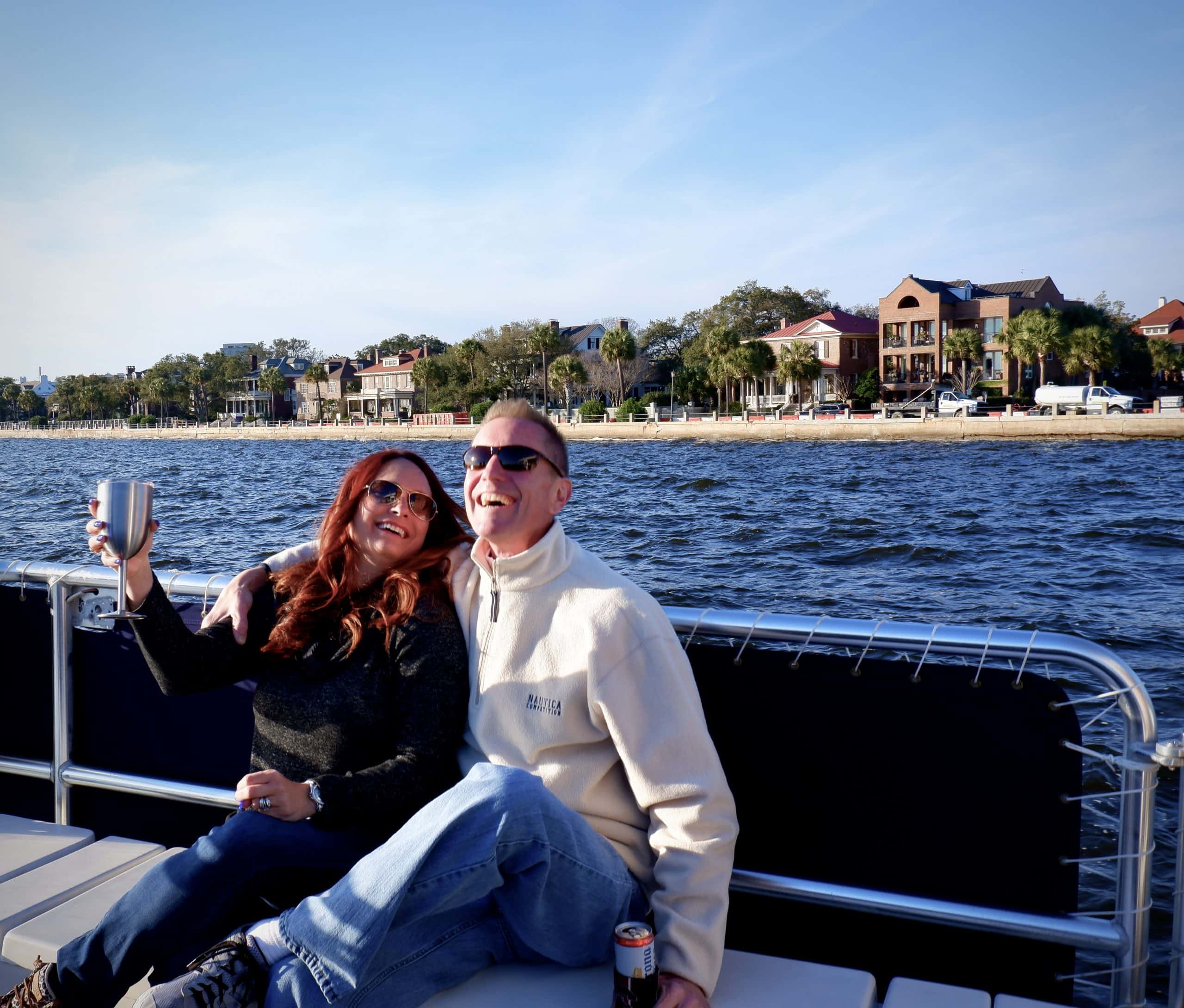 Couple pictured on the boat, laughing, with The Battery in the background. Party boat rental Charleston, SC