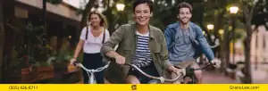Three young adults smiling and riding bicycles down a tree-lined street, with the Grano Law Offices, P.C., logo and phone number overlay.