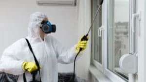 Contrôleur de pest control en combinaison de protection, utilisant un pulvérisateur pour traitement contre les nuisibles dans un bâtiment résidentiel ou commercial.