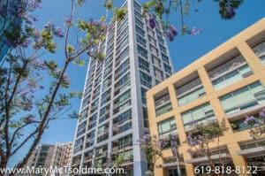 Low-angle exterior view of the modern high-rise condominium building at 321 10th Ave, framed by blooming purple Jacaranda trees under a bright blue sky.