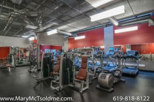 Modern fitness center at 321 10th Ave with industrial-style ceilings, cardio machines, strength training equipment, and vibrant red accent walls.