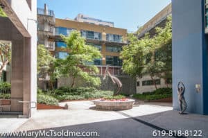 Modern multi-story condominium complex at 321 10th Ave with a sunny outdoor courtyard featuring a central sculpture, lush greenery, and contemporary architecture.
