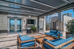 Industrial-chic rooftop lounge at 321 10th Ave featuring vibrant blue sofas with wooden frames, a slatted metal pergola for shade, and an outdoor television area for entertainment.