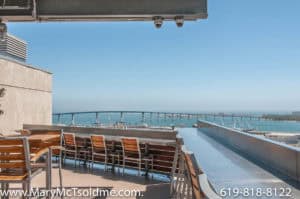 Panoramic view of the Coronado Bridge and San Diego Bay from the rooftop lounge at 321 10th Ave, featuring modern outdoor bar seating and wooden dining tables.