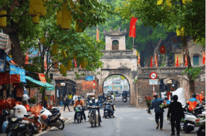 Bustling street scene in Hanoi with scooters, colonial buildings, and local markets.