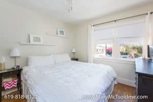 Bright bedroom at 3164 Thorn St in North Park with white bedding, hardwood floors, minimalist wall shelves, and natural light from large windows.