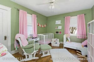Green nursery at 3164 Thorn St in North Park with pink curtains, a white crib, a toddler bed, and a comfortable rocking chair with ottoman.