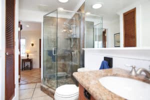 Primary bathroom at 3704 Maple St in North Park featuring a glass-enclosed walk-in shower with stone tile, a granite vanity, and louvered wood closet doors.