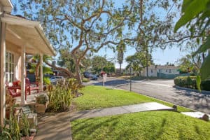 Front porch and manicured lawn at 3704 Maple St in North Park with red Adirondack chairs and a view of the quiet neighborhood street under a mature tree canopy.