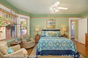 Bright Craftsman bedroom at 3758 31st Street in North Park featuring sage green walls, large windows with wood blinds, a blue patterned bedspread, and comfortable beige armchairs.