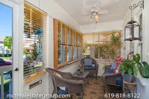 Enclosed sunroom at 3758 31st Street in North Park featuring white wood-paneled walls, large windows with wood blinds, a ceiling fan, and a cozy seating area with wicker furniture and blue cushions.