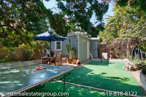 Cozy sage green cottage backyard in North Park, San Diego, featuring a ping pong table, outdoor dining area with a blue umbrella, and lush greenery at 3758 31st Street.