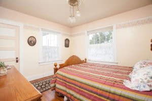 Classic bedroom at 2873 Upas St in North Park featuring a wood bed frame with striped bedding, two large windows with lace curtains, and vintage oval-framed portraits on the wall.