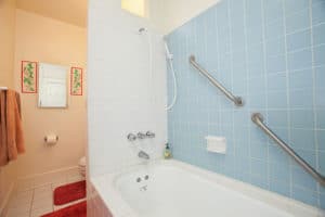 Brightly lit bathroom at 2873 Upas St in North Park featuring a white tiled bathtub, light blue wall tiles with safety grab bars, and a classic shower-tub setup.