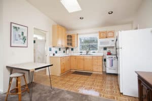 Sun-drenched kitchen at 2873 Upas St in North Park featuring a large skylight, light wood cabinets with teal tile accents, and a small dining nook with a hairpin-leg table.