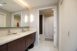 Modern primary bathroom at 321 10th Ave with a wide dual-sink vanity, marble counters, and a pocket door opening to a bright shower and toilet area.