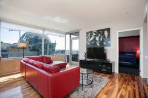 Bright urban condo at 321 10th Ave with floor-to-ceiling windows overlooking the San Diego Central Library dome, featuring a red leather sofa and hardwood floors.