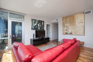 Modern living room at 321 10th Ave featuring a vibrant red leather sectional, polished hardwood floors, and a large abstract canvas painting.