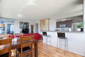 Modern open-concept living area at 321 10th Ave featuring a wood dining table, a vibrant red leather sofa, and a kitchen with a granite breakfast bar and dark wood cabinetry.
