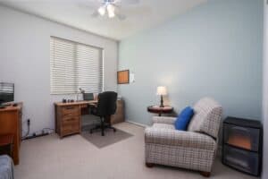 Functional home office setup in a guest bedroom at 5235 Beachfront Cove Unit 102, featuring a wooden desk, office chair, and natural light from a window with custom blinds.