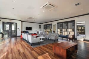 Modern community lounge at featuring hardwood floors, gray armchairs, a wall-mounted TV, and large windows.