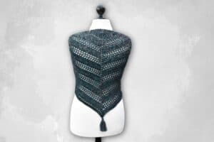 Das Häkeltuch New Orleans in der blauen Farbvariante mit Quaste auf einer Schneiderbüste.