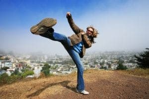 Young woman fooling around doing high kick ontop of the Kite Hill, San Francisco, California, USA.