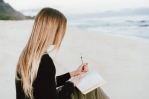 Wees helder over je intenties, vrouw zit op het strand en schrijft haar intenties op in een notitieboekje