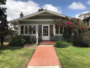 Exterior of a charming green Craftsman bungalow at 3758 31st Street, featuring a red brick walkway, a wide front porch with white trim, and vibrant pink bougainvillea.
