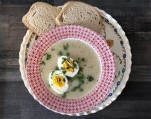 A bowl of white borscht soup with eggs and bread on a plate.