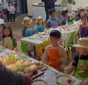 Children in party hats enjoy a birthday celebration with cake and decorations.