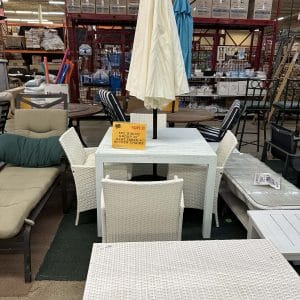 Outdoor patio furniture set with white chairs and a table under a closed umbrella.