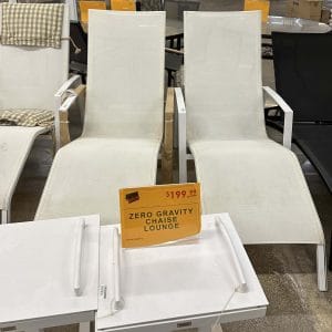 Two white lounge chairs with a sale sign in a store.
