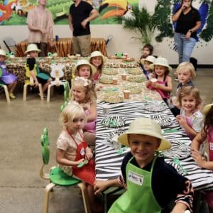 Children sitting around a long table for a party with animal-themed decorations.