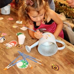 A girl painting a white watering can at a table.
