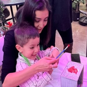 A woman helps a young boy open a gift with excitement.
