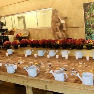 A festive table setup with white cups and red flowers, featuring a large teddy bear.