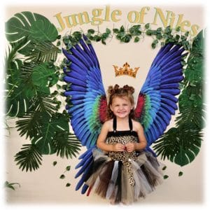 A young girl dressed as a colorful butterfly in front of a jungle-themed backdrop.