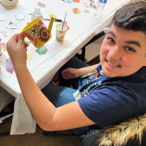 A boy proudly shows a colorful card while sitting at a table with snacks.